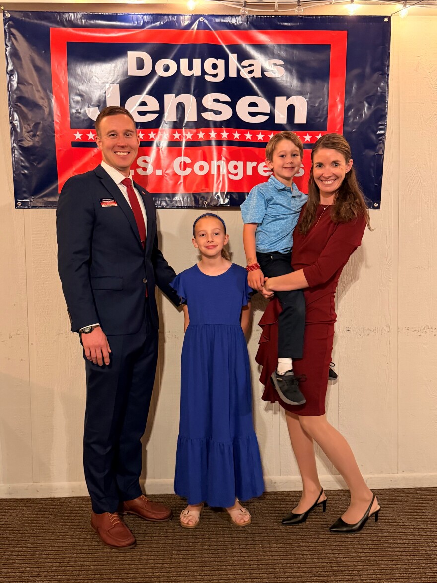 A family is standing in front of a sign that says Douglas Jensen U.S. Congress