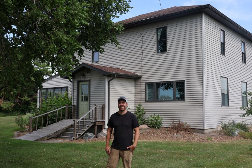 A man in his forties wearing a black shirt stands in front of his home, which has stood for over a hundred years.