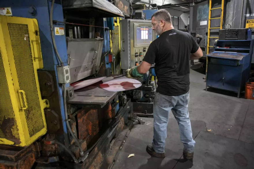 Mill operator Matt Fraser feeds disks of hot metal into a roller at the Zildjian cymbal factory.