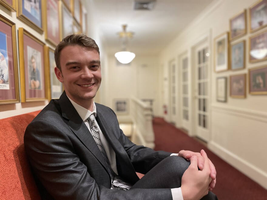 man in suit in hallway, seated on bench