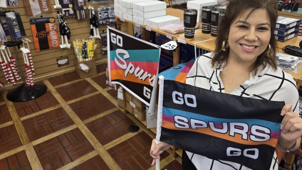 Lorena Ortega, the sales and marketing manager at Dixie Flag & Banner Company, holds up one of their best sellers—a Spurs car flag