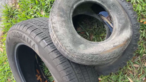 Three black tires filled with water are lying out on the grass.