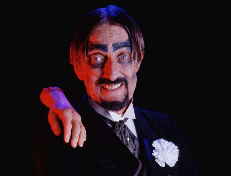 Man dressed in a costume with black suit and a severed hand on his shoulder 