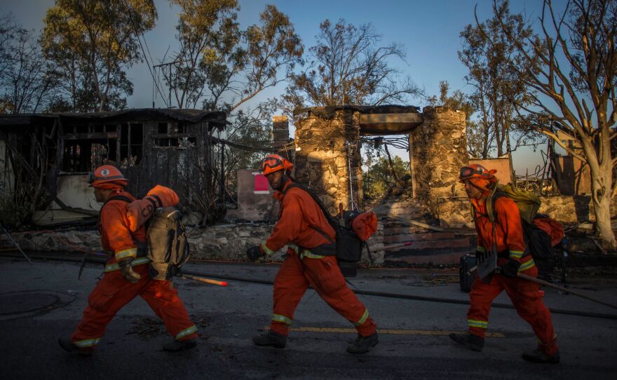 Inmate firefighters walk past a burnt building Monday in Brentwood, Calif., where the Getty Fire destroyed several homes and forced a partial shutdown of the busiest highway in the country.