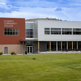 A two-story modern building, with lots of windows and a green lawn in front. 