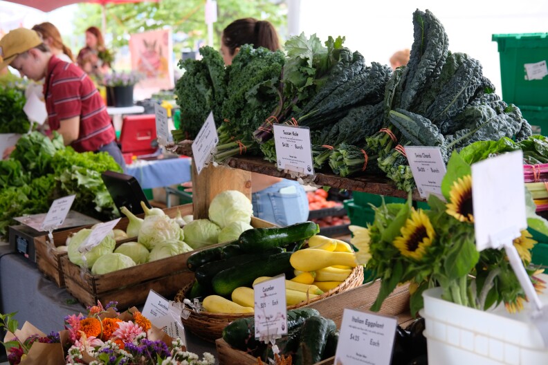 Green Things Farm Collective stand at Saturday's Ann Arbor Farmer's Market. Flowers and vegetables are displayed on a table in front of workers, with customers browsing the stand
