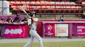 London Studer wears a gray baseball uniform and looks to the sky as she prepares to swing a bat.