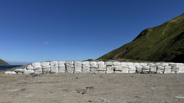 off white cubes are stacked on flat ground covered in dirt. green mountains are in the background