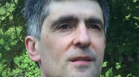 A man with short grey hair, wearing a blue polo shirt