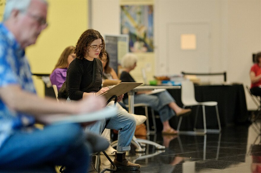 People sit in the atrium of Kemper Museum of Contemporary Art and draw on paper.