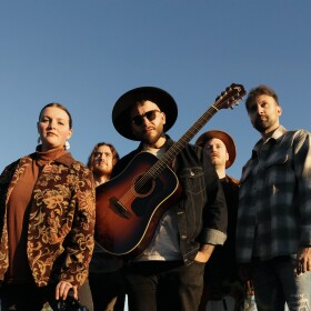 Photo of VOYAGR, with the man in the middle wearing a guitar around his body