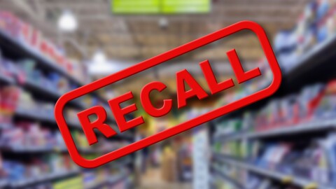 Blurry interior of a grocery store aisle behind large red Recall text