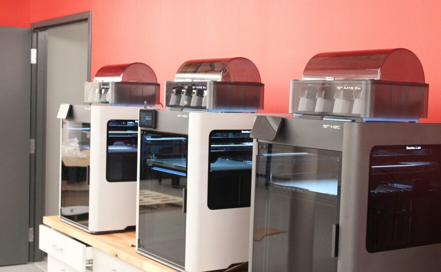 Three 3D printers set in a row atop a set of drawers.
