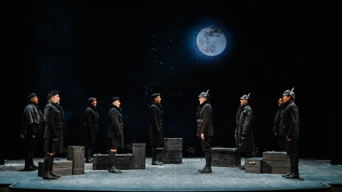 Men in World War I black uniforms face each other, standing on a stage.
