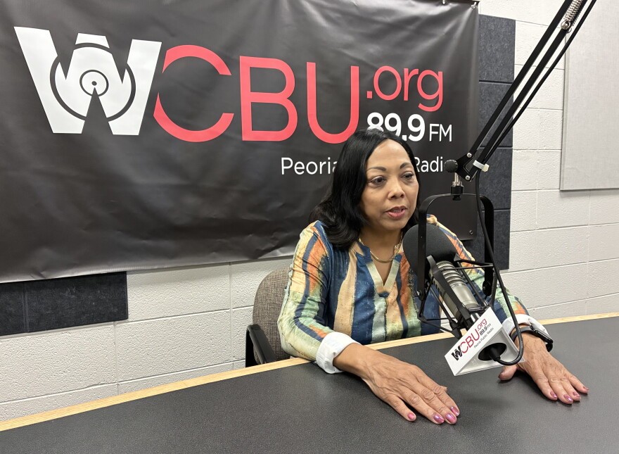 A woman speaks into a radio microphone in front of a WCBU 89.9 FM banner.
