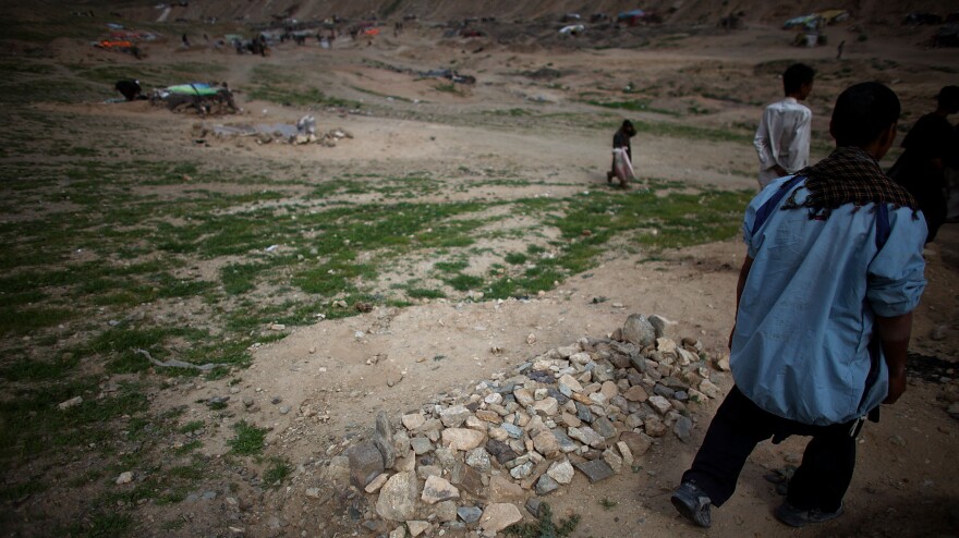 A man walks past a fresh grave in the Kamar Kulagh slum outside of Herat.