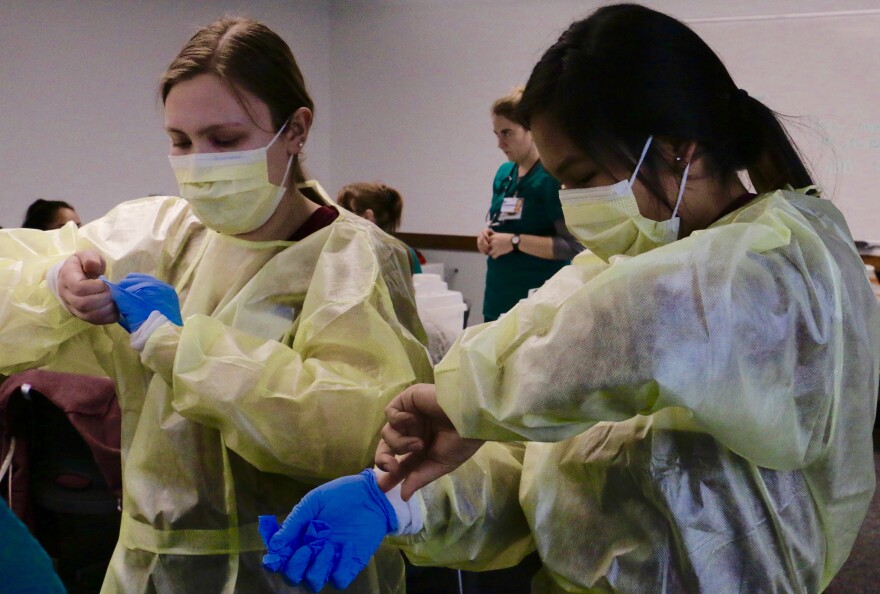 From left to right: Bethel Regional High School senior Caitlyn Twito and Tuntutuliak junior Katya John learn how to properly remove gloves after pretending to nurse a wounded patient.