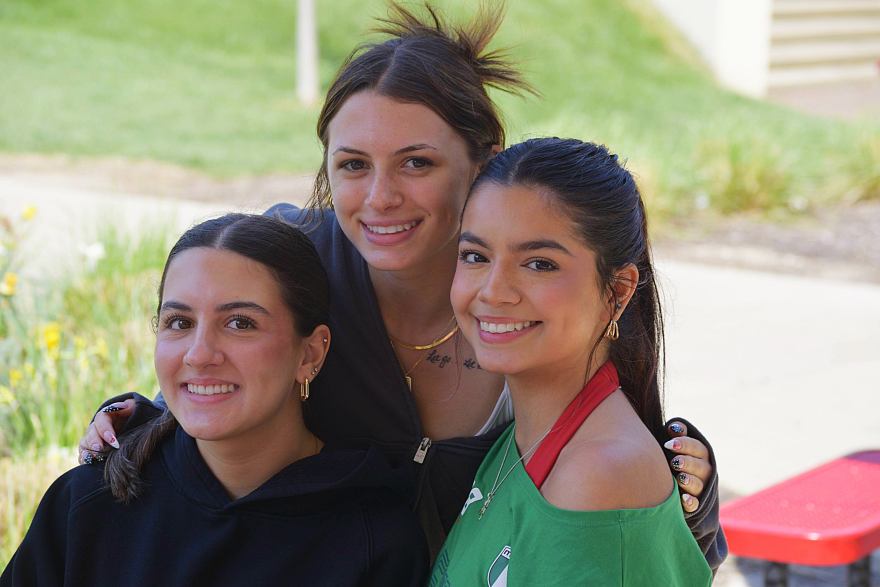Three women smiling together on a sunny day.