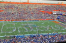 Gator football field. Band is on the field, using their bodies to create the word Gators. Some of the campus is seen in the background.