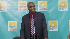 A smiling man in a dark suit against a blue Fla Dept of Health backdrop