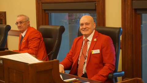 Two men sit at a table in red coats.