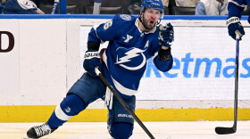 Hockey player in a blue uniform with a lightning bolt on the front with his knee on the ice and fist in the air celebrating