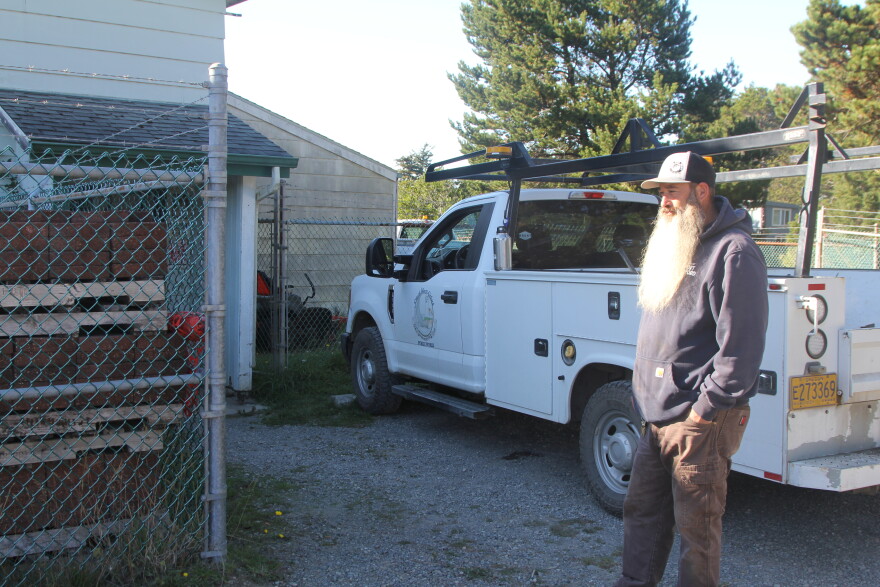 A man stands in front of a white pickup truck in the driveway of an industrial building.