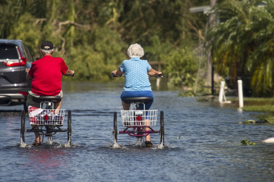 TOPSHOT - Two retirees ride tricycles through a flooded street at the Enchanted Shores manufactured home park in Naples, Florida, on September 11, 2017 after Hurricane Irma hit Florida. (Photo by NICHOLAS KAMM / AFP) (Photo credit should read NICHOLAS KAMM/AFP via Getty Images)