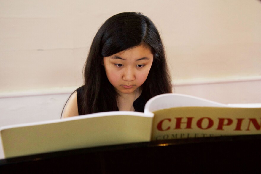 A young girl looks at a Chopin book at a piano.