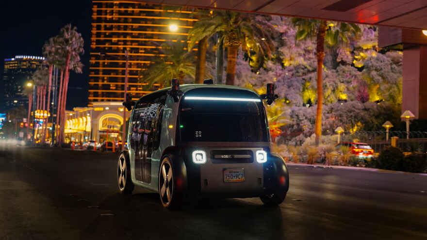 A black and green robotaxi going down the road with casinos in the background