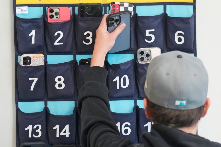 FILE - A ninth grader places his cellphone into a phone holder as he enters class at Delta High School, Friday, Feb. 23, 2024, in Delta, Utah. (AP Photo/Rick Bowmer, file)