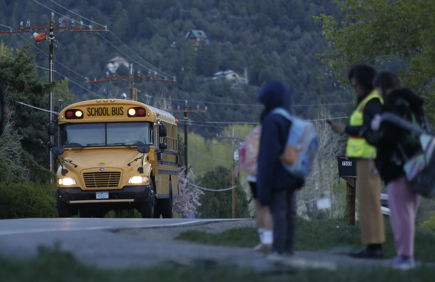 Children wait for their school bus with E.B., a volunteer who arrives at dawn to watch for immigration officials as the kids head off to school in Durango on Monday, April 6, 2026.