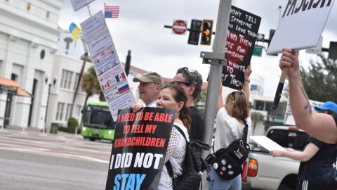 People stand along South Orange Avenue in downtown Orlando on Saturday, holding signs as passing drivers honk in response during the No Kings Day rally.