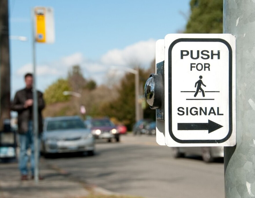 Crosswalk on road with cars with a 'push for signal' sign featuring symbol of person walking