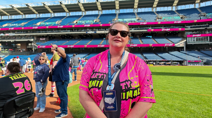 A woman with sunglasses wearing a pink Party Animals jersey and a field pass around her neck stand on the field at Progressive Field.