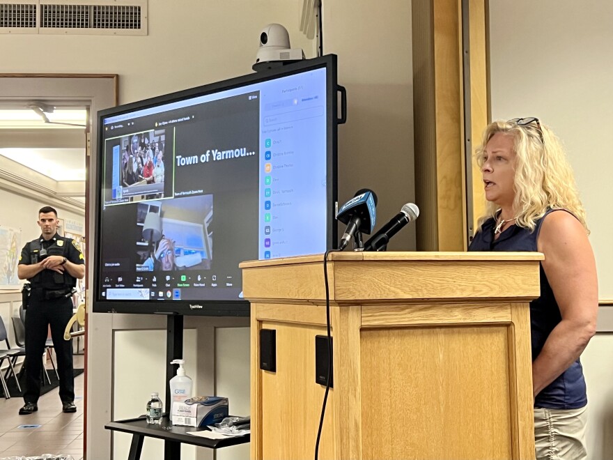 Cheryl Ball speaks to the Yarmouth Board of Selectmen Tuesday as a police officer looks on. Ball organized a Facebook group to oppose the Healey administration's decision to shelter migrants in Yarmouth.