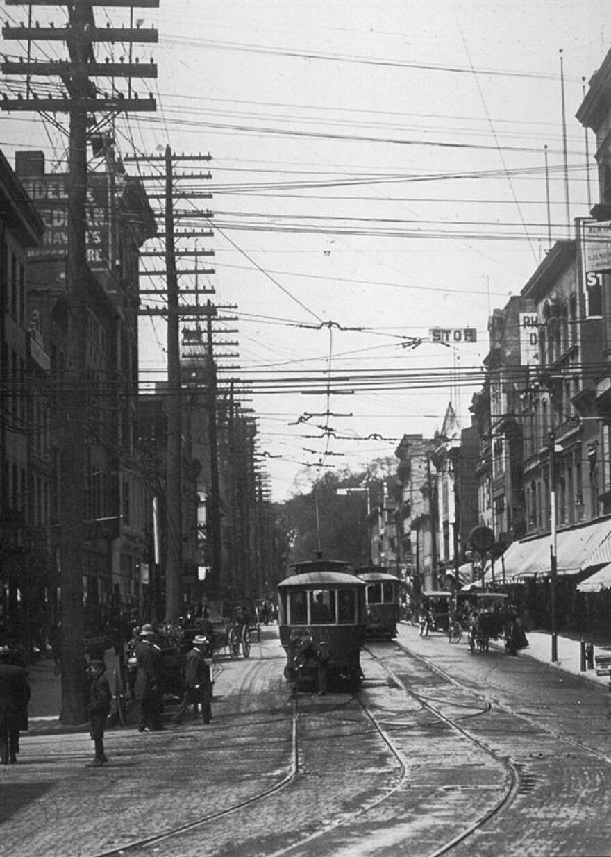 A streetcar on New Haven's Chapel Street in the 1910s. The conductor manually switched tracks using a pry-bar. This image shows how streetcars were integrated into the fabric of the street. Cars were parked on the street below a dense network of catenary wires.