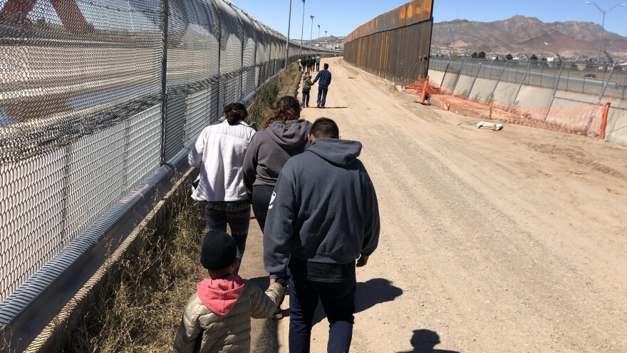 Migrants trudge along the border fence to a waiting bus after turning themselves in to the Border Patrol at the U.S.-Mexico border near El Paso, Texas.