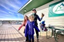 A woman and three young kids dressed in winter gear on an outdoor patio.