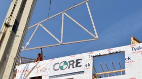 A construction worker guides a signed truss hoisted up by a crane into place on the fourth floor of the Madison North Apartments development. The apartments for people experiencing homelessness are expected to open next February.