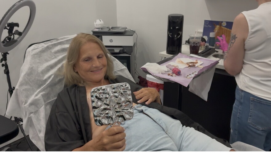 Judy McRae, a breast cancer survivor, gets a look at the work of Christie Laney, registered nurse and owner of ‘The Inked Daisy,’ after she tattooed an areola on her breast.