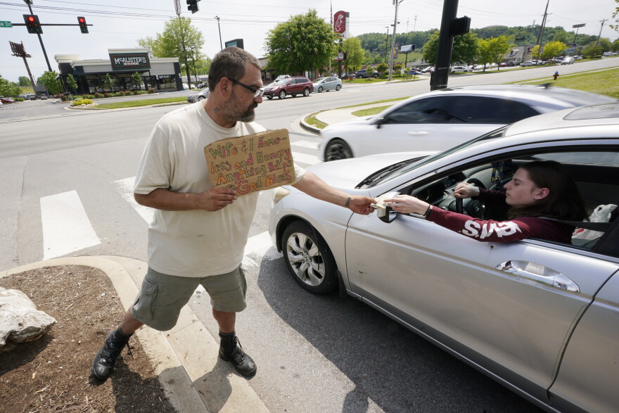 Adam Atnip, who is homeless and lives in his car, accepts money from a driver as he panhandles on May 10, 2022, in Cookeville, Tenn. Tennessee is about to become the first U.S. state to make it a felony to camp on local public property such as parks.