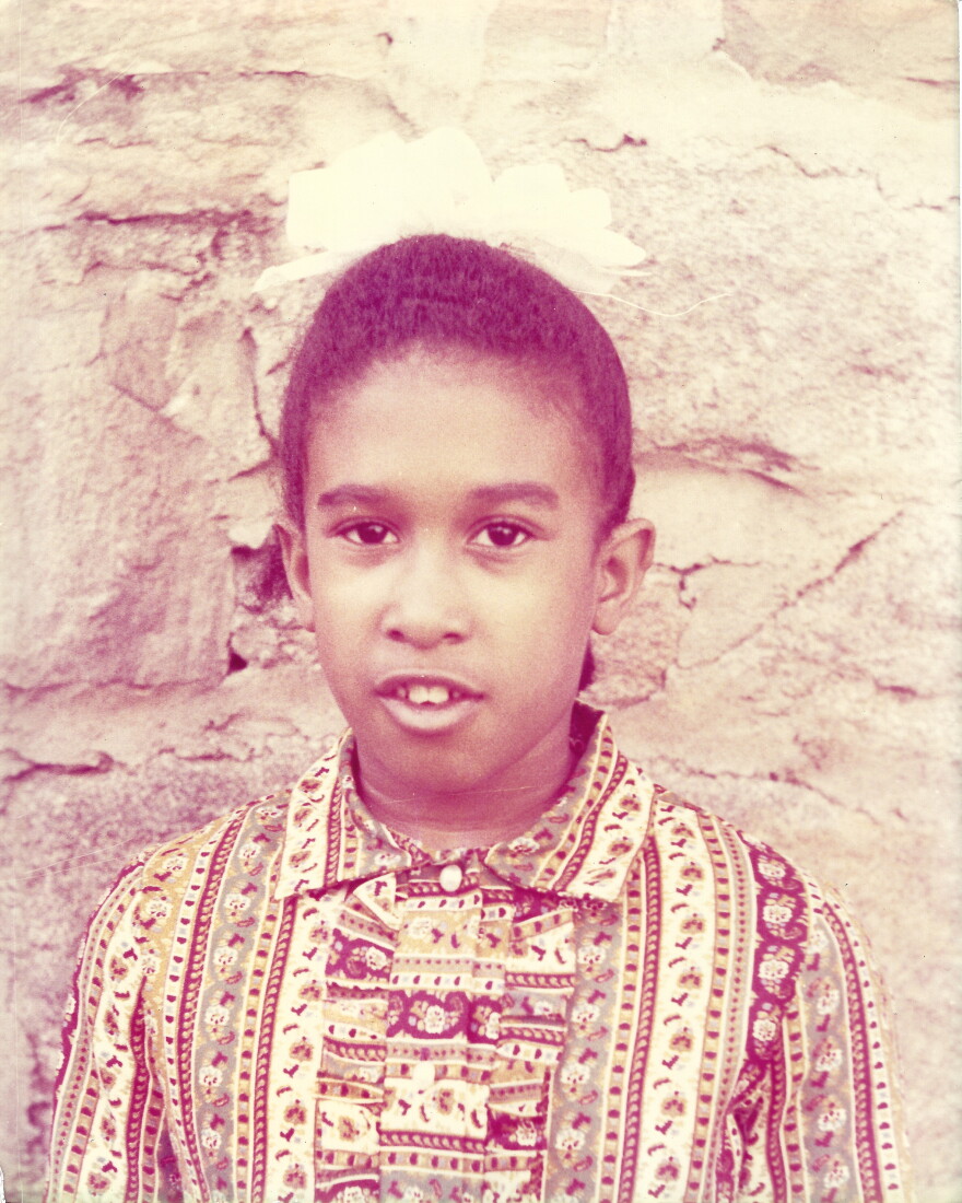 Portrait of a little Black girl standing in front of a stone wall.