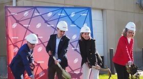 Four people dig into a pile of dirt for a groundbreaking ceremony.