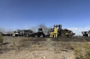Firefighters hose water on burnt tractor-trailers and cars enveloped in smoke on a rural, desert highway in Arizona.