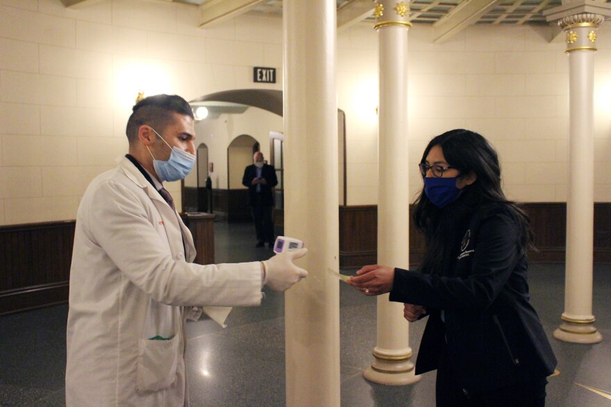 Alex Mchawrab, a pharmacist deputized to take the temperatures of lawmakers as they entered session Tuesday, takes a sticker allowing reentry from Democratic Rep. Vanessa Guerra. After lawmakers checked in for session, they were encouraged to leave before returning hours later for a voice vote.