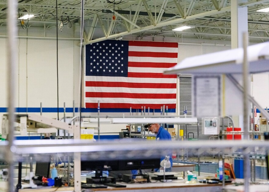 Large American flag is displayed along the back wall of a manufacturing room as an employee stands next to a desk