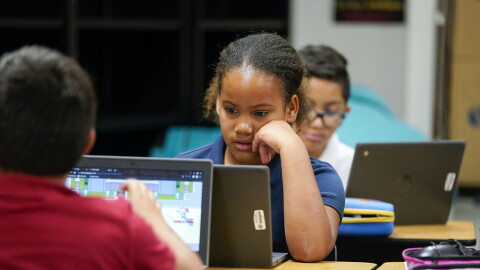 A young child sits by a computer.