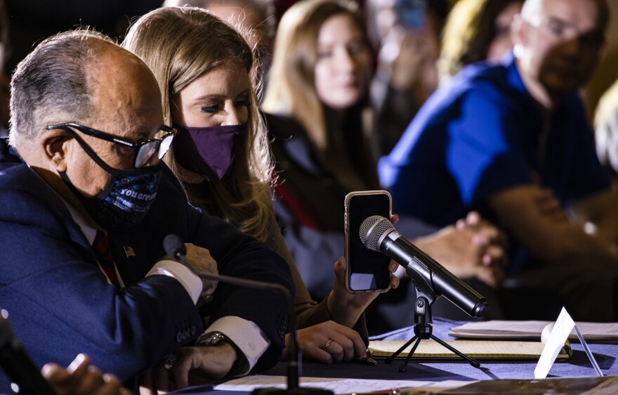 Jenna Ellis, a member of President Trump's legal team, holds up a phone to the microphone so Trump can speak Wednesday during a public hearing in Gettysburg, Pa., to discuss alleged election issues.