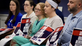 A row of nurses, patients and healthcare professionals hold signs that say, "Save Grady Memorial Maternity."